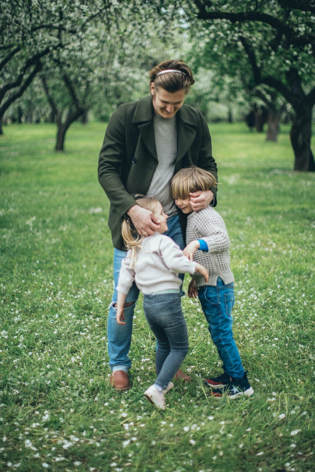 Pai abraçando os dois filhos em um parque
