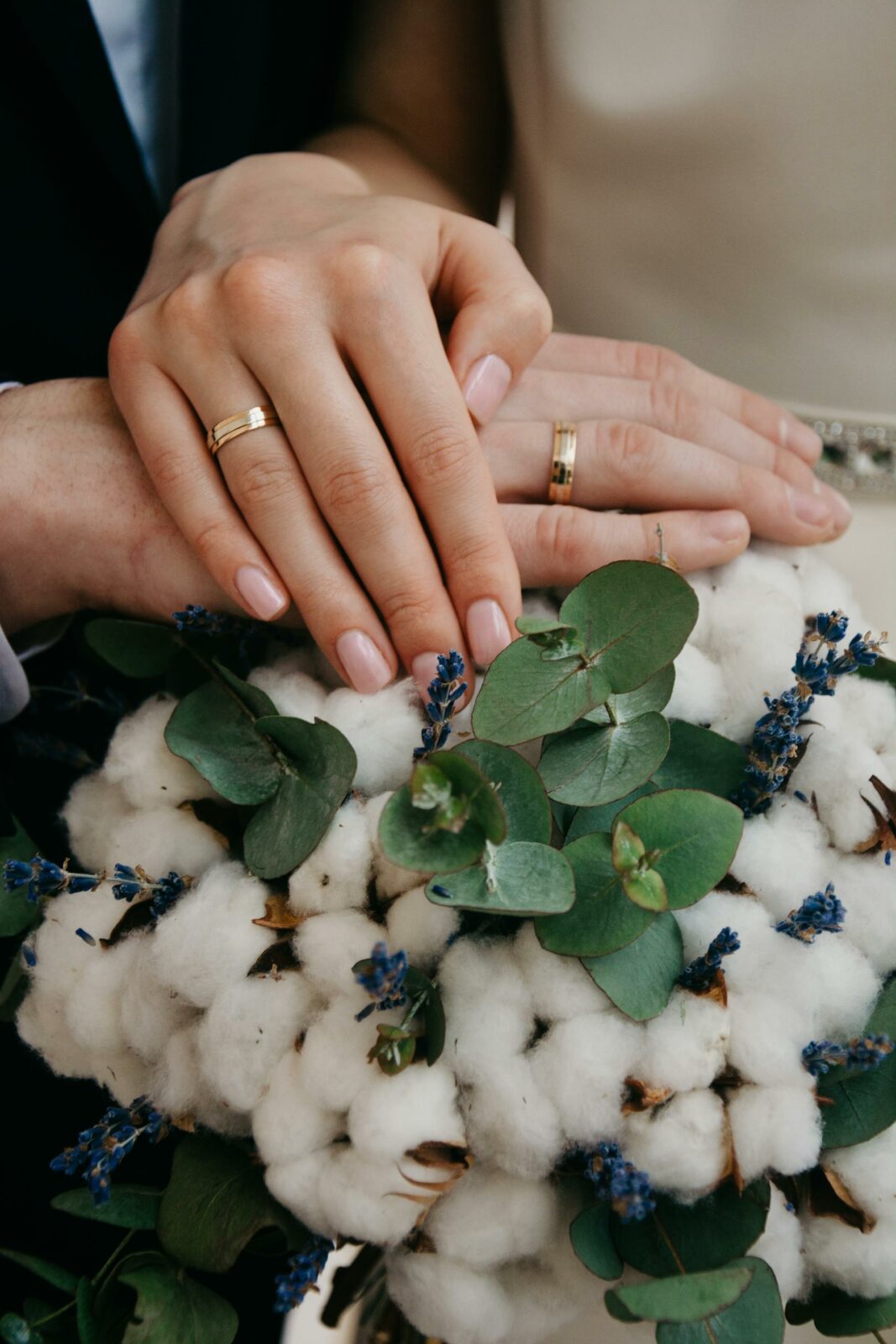 Mãos de noivos com alianças sobre um buquê de flores