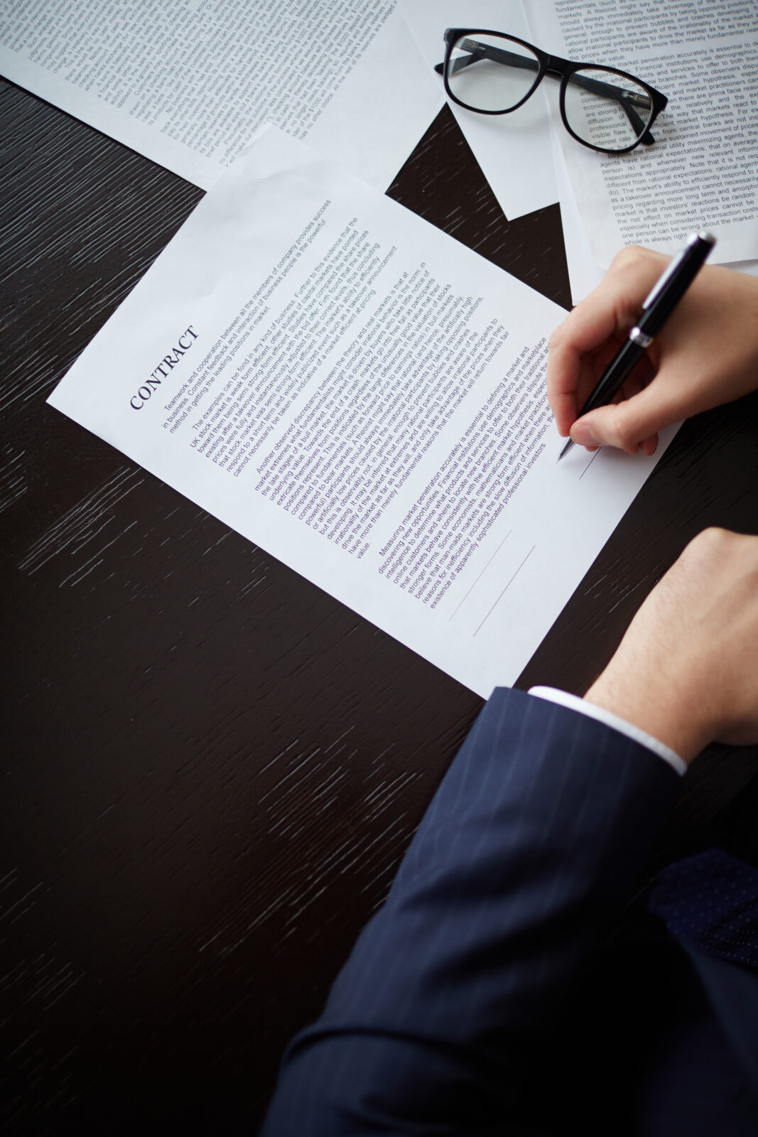 Mão de empresário com caneta assinando contrato de trabalho no escritório